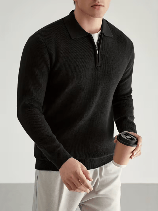 Zwarte half-zip heren trui met opstaande kraag, gedragen casual met lichtgrijze broek en koffiebeker.