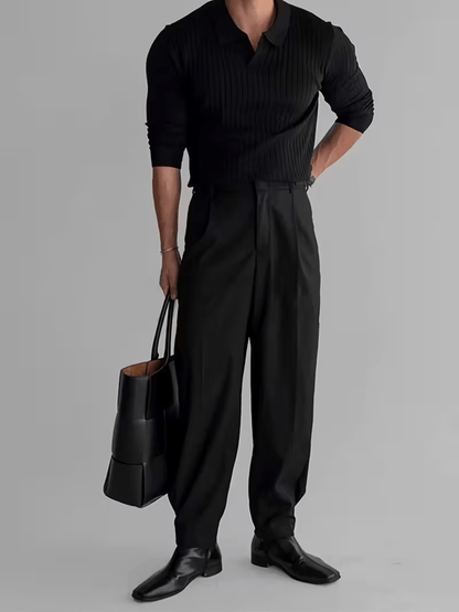Zwarte ribgebreide polo trui met lange mouwen, gedragen met zwarte pantalon, leren tas en nette schoenen.
